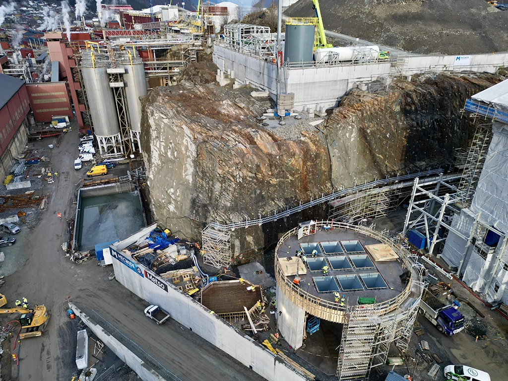 Baustelle mit Felsabtrag und Industriegebäuden in verschiedenen Höhen.